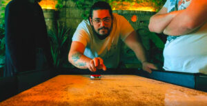 Un joueur en plein lancer sur une table de shuffleboard Chez Freeing Café